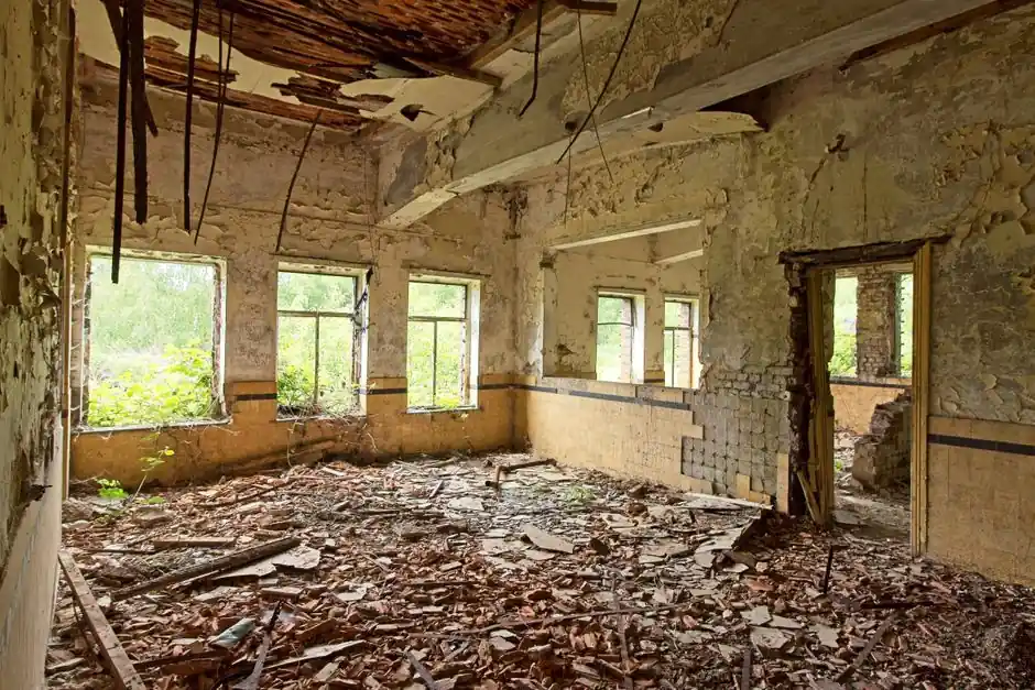 A dilapidated room with broken walls, windows, and debris on the floor, showing signs of decay and neglect.