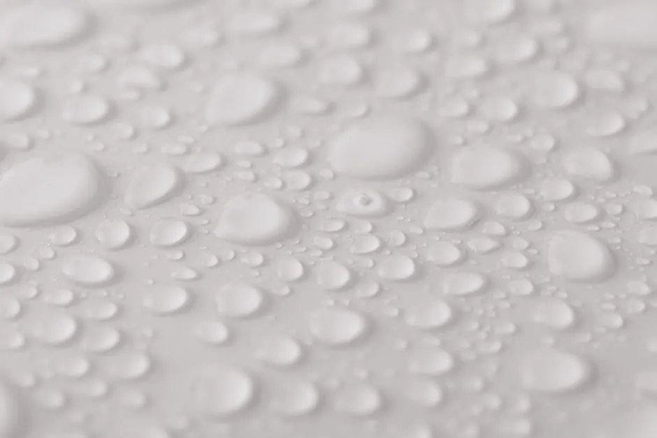 Closeup from above of clean white background with transparent glassy water drops of different sizes and shapes with blurred sides